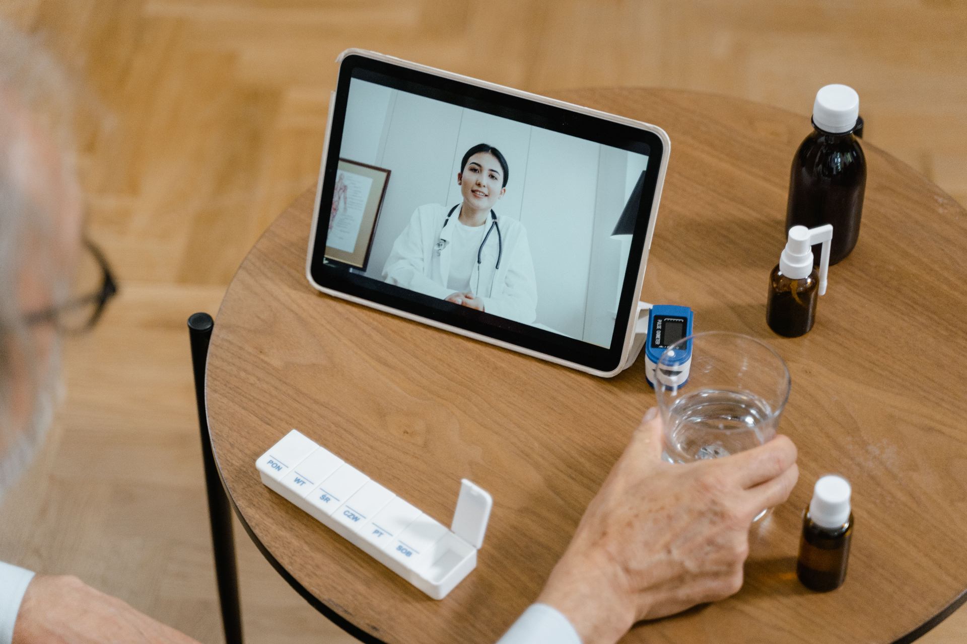 Patient âgé en téléconsultation avec sa médecin sur tablette, à côté d'un oxymètre et d'un pilulier